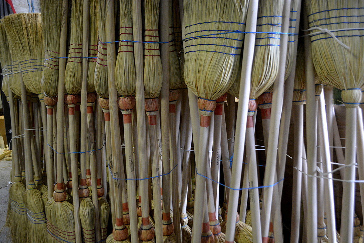 Plusieurs balais de paille de sorgho alignés à l'atelier